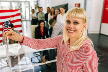 Young blonde woman voter placing ballot in ballot box polling place in America.