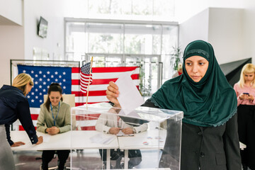 Muslim voter with hijab placing ballot in ballot box polling place in America.