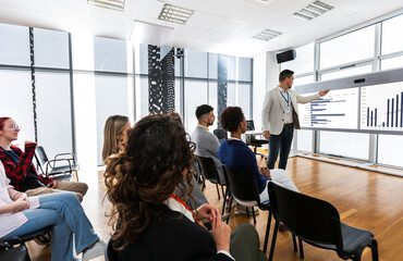 Male CEO standing in front of a multiracial group of colleagues. Multimedia classroom with smart board and graphics on them. - Powered by Adobe