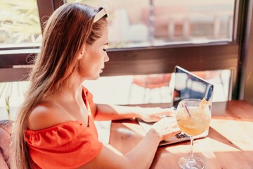 Woman works on laptop in a sunny cafe, glass of juice nearby. The setting is modern, with natural...