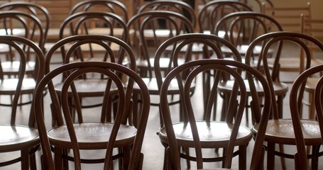 Empty wooden chairs in a hall in concepts such as abandonment, emptiness, solitude, waiting, or anticipation gatherings, events, or meetings yet to happen. Chairs indoor symbolize pause in activity.