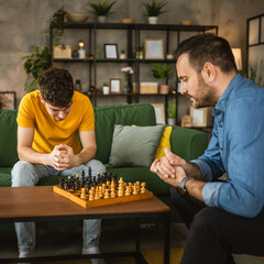 Two male friends brothers play chess together at home