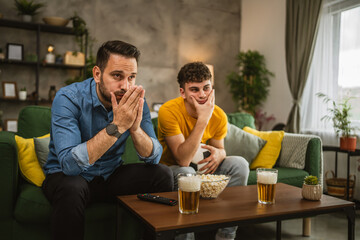Two man friends are disappointed while watch football match at home
