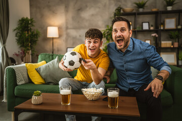 Young and adult man friends watch football match and cheer at home