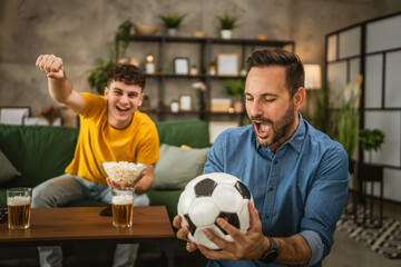 Young and adult man friends watch football match and cheer at home