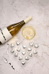 Heart made with delicious chocolate candies and champagne on white marble table, flat lay
