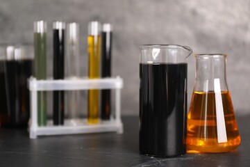 Beakers, flask and test tubes with different types of oil on grey textured table, closeup