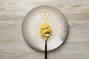 Heart made with spaghetti and fork on light wooden table, top view