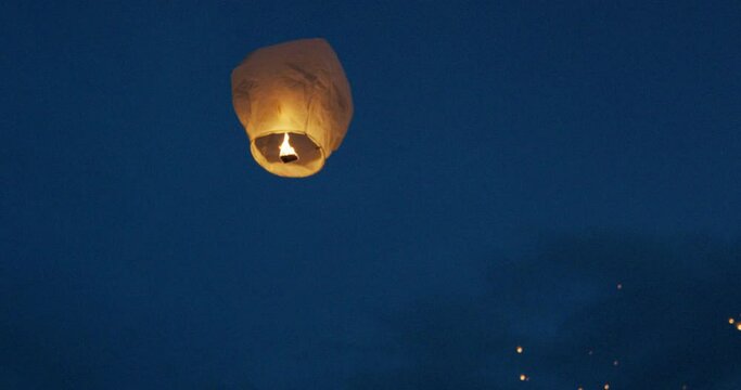 Releasing glowing Chinese lantern into sky at dusk