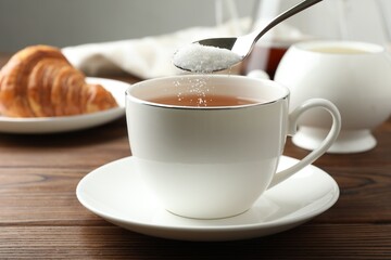 Adding sugar into cup of tea at wooden table, closeup
