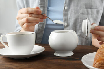 Woman adding sugar into cup of tea at wooden table, closeup