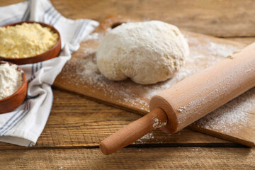 Rolling pin, flour and dough on wooden table, closeup