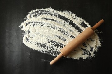 Scattered flour and rolling pin on black table, top view