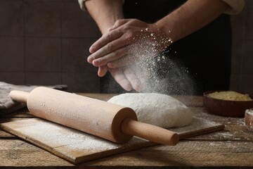 Man sprinkling flour over dough at wooden table, closeup