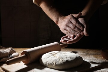 Man sprinkling flour over dough at wooden table, closeup