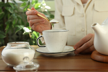 Woman adding sugar into aromatic tea at wooden table indoors, closeup