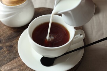 Pouring milk into cup with tea on light table, closeup