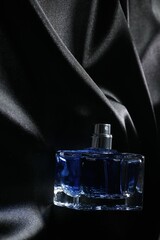 Luxury men's perfume in bottle on black satin fabric, top view. Space for text