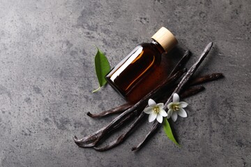 Vanilla pods, flowers, leaves and bottle with essential oil on grey textured table, flat lay. Space for text