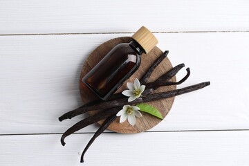 Vanilla pods, flowers, leaf and bottle with essential oil on white wooden table, top view