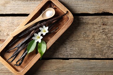 Vanilla pods, flowers, leaves and spoon with sugar on wooden table, top view. Space for text