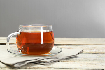 Aromatic tea in glass cup and napkin on wooden table. Space for text