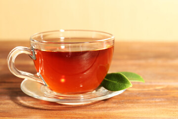 Aromatic tea in glass cup and green leaves on wooden table