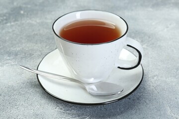 Aromatic tea in cup and spoon on grey table