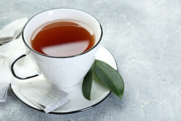 Aromatic tea in cup, teabags and green leaves on grey table