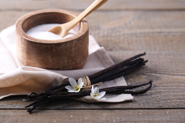 Vanilla pods, sugar in bowl and flowers on wooden table, closeup