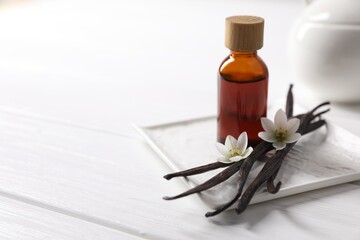 Vanilla pods, essential oil and flowers on white wooden table, space for text
