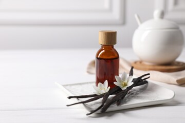 Vanilla pods, essential oil and flowers on white wooden table, space for text