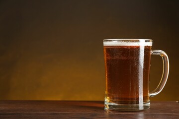 Mug with fresh beer on wooden table against dark background. Space for text