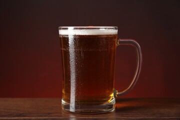 Mug with fresh beer on wooden table against color background