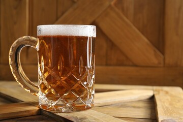Mug with fresh beer on wooden crate, closeup. Space for text