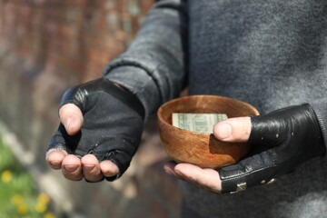Poor homeless man holding bowl with donations outdoors, closeup