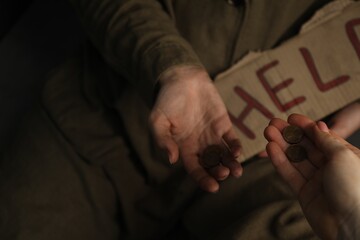 Woman giving coins to homeless with help sign, closeup. Charity and donation