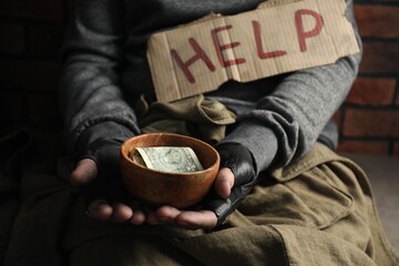 Poor homeless man with help sign holding bowl of donations, closeup