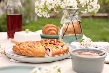 Stylish table setting with beautiful spring flowers, fruit drink and pie in garden