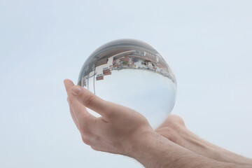 View of beautiful city street, overturned reflection. Man holding crystal ball against sky, closeup