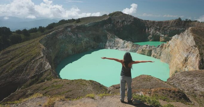 Woman enjoy volcano mountain crater edge. Volcanic Kelimutu blue crater lake. Travel destination. Beautiful wild landscape. Female tourist on summer vacation. Lifestyle holiday concept. Back view