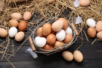 Fresh chicken eggs and dried straw on black wooden table, flat lay