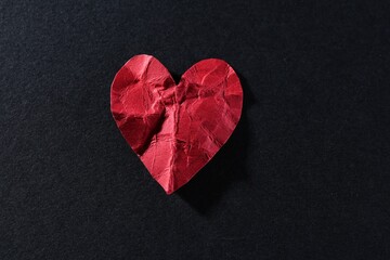 Red crumpled paper heart on black background, top view. Breakup concept