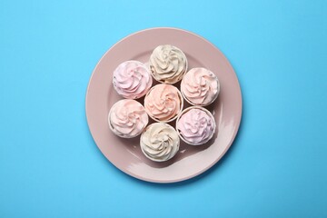 Plate with tasty cupcakes on light blue background, top view