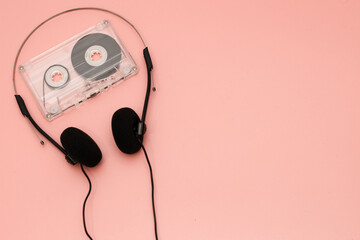 A pair of 1990's style headphones and and cassette tape on a pink background retro vintage music...