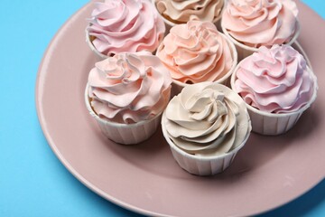 Plate with tasty cupcakes on light blue background, closeup