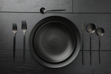 Stylish setting with cutlery and plates on black wooden table, flat lay