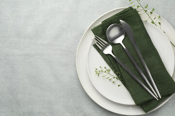 Stylish setting with cutlery, leaves and plates on grey table, top view. Space for text
