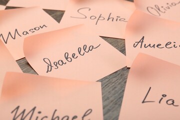 Paper stickers with different names on wooden table, closeup. Choosing baby's name