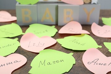 Paper stickers with different names on wooden table, closeup. Choosing baby's name